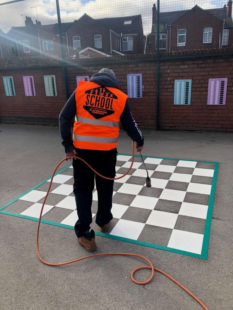 A member of our refurbishment and repairs team cleaning a large chess board playground marking design to improve safety